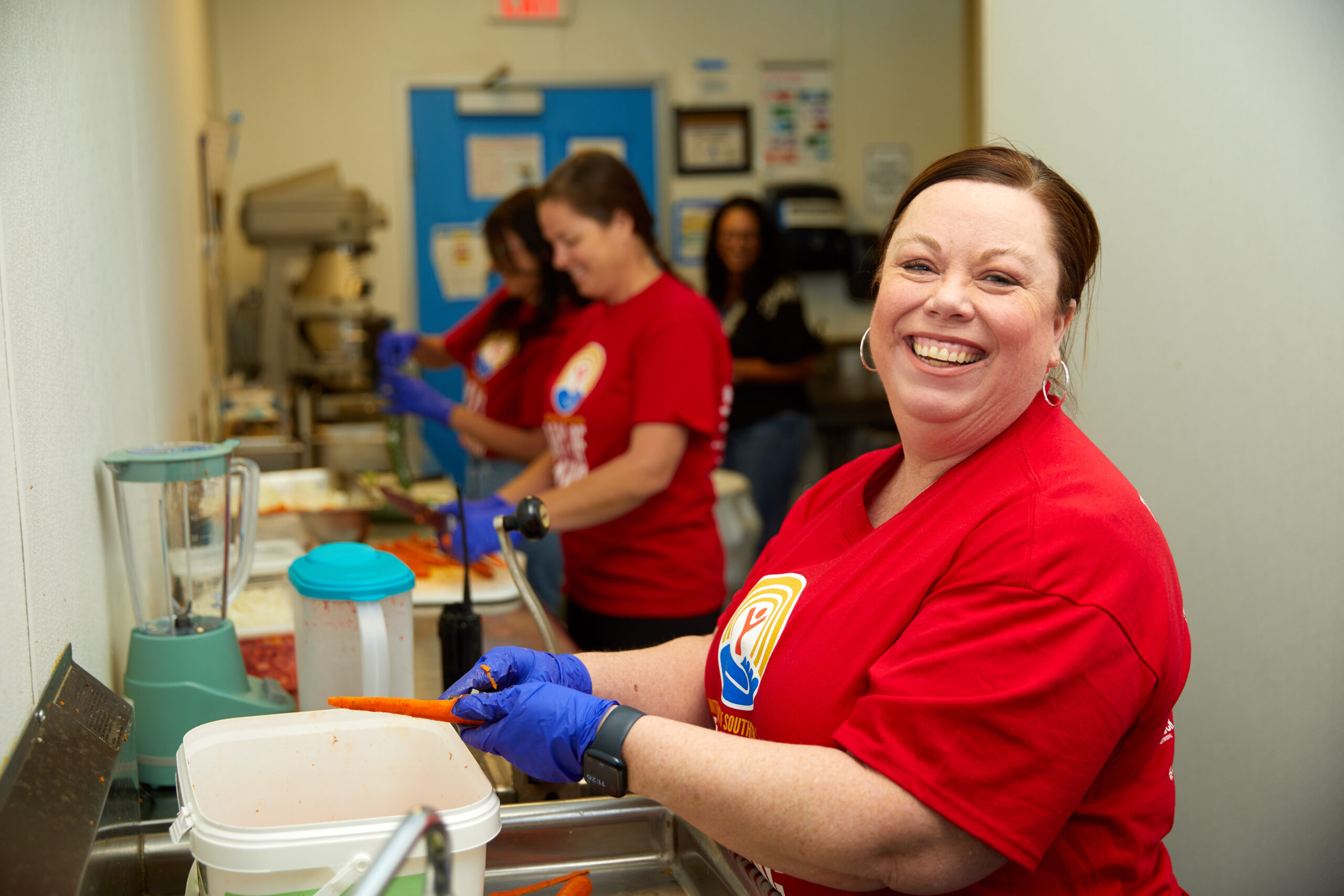 A smiling woman in a red United Way t-shirt prepares meals for families in need.